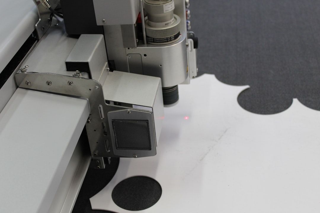 En maskin skär ut former ur vitt material, med en röd laserprick.