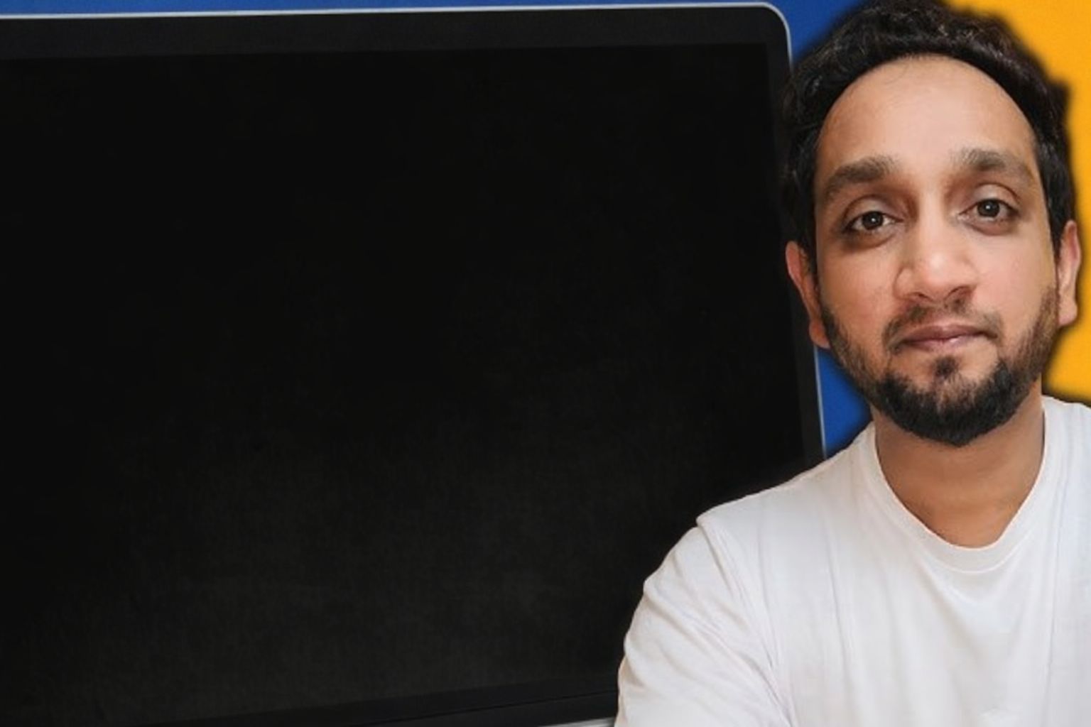 En man med skägg och vit t-shirt tittar in i kameran bredvid en svart skärm.
